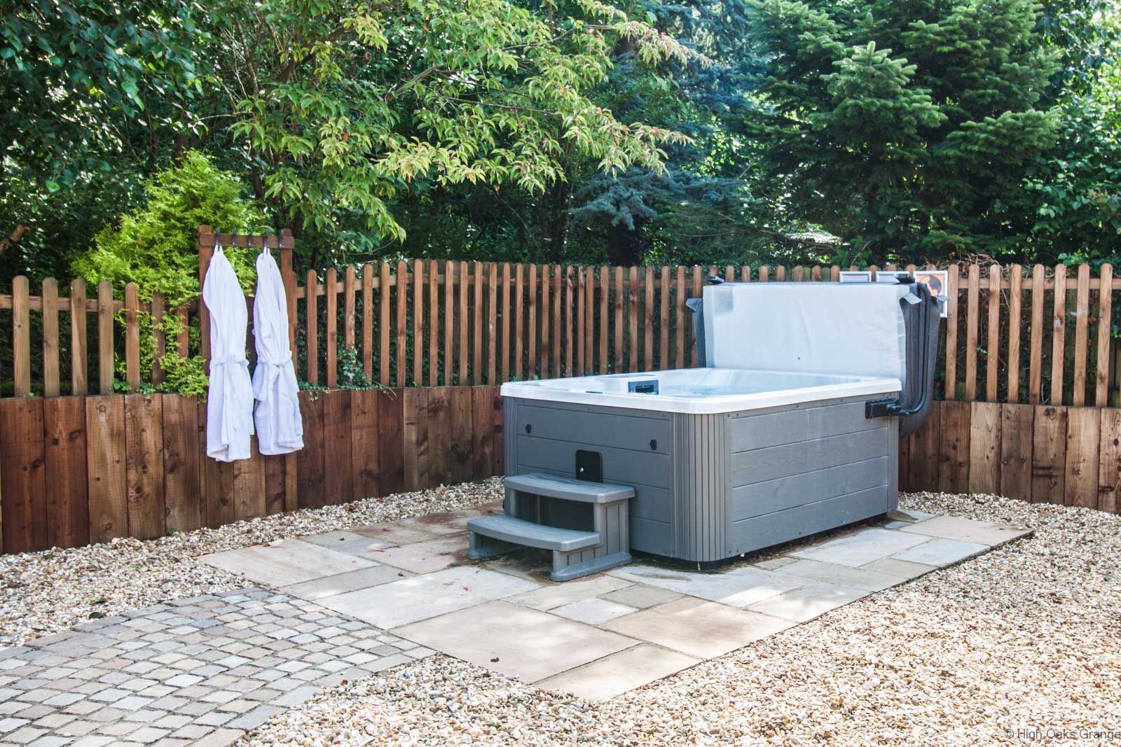 A hot tub in a backyard with a wooden fence, gravel ground, and a tiled patio.
