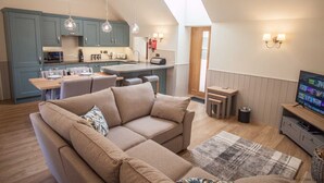 Ein gemütliches Wohnzimmer mit Sofa, Fernseher und einer Küche im Hintergrund.