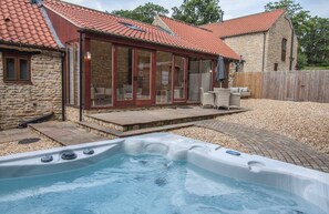 Un bain à remous dans un jardin, avec une maison en pierre et un patio couvert.