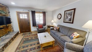 Ein Wohnzimmer mit Sofa, Sessel, Couchtisch, Fernseher und einem gemusterten Teppich.