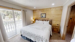 Ein Schlafzimmer mit einem Holzkopfteil, einem großen Bett mit floralem Überwurf, einem Nachttisch mit Lampe und einem Balkon mit Geländer.