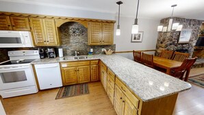 Eine Küche mit Granit-Arbeitsplatten, Holzschränken, einer Stein-Spritzschutzwand, einem Einbauofen und einem Essbereich mit Steinwand und Holzsesseln.
