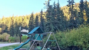 Ein Spielplatz mit Rutsche und Schaukel, umgeben von einem bewaldeten Gebiet.