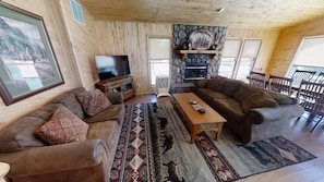 A cozy living room with a fireplace, wooden walls, and a large TV.