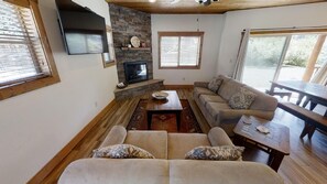 Una sala de estar acogedora con chimenea de piedra, un sofá, una mesa de centro y una mesa de comedor.