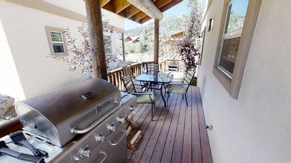 Un patio al aire libre con una parrilla, una mesa con sillas y vistas del paisaje circundante.