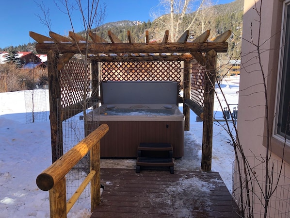 Relax in a hot tub on a wooden deck with a lattice roof, surrounded by a metal fence.