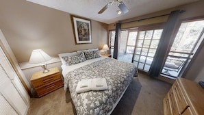 Une chambre à coucher comprenant un lit, une table de chevet, une lampe, une fenêtre avec vue et un ventilateur de plafond.