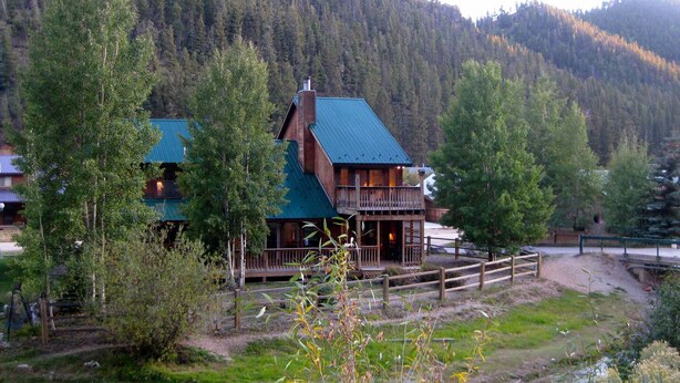 Une cabane dotée d’un toit végétalisé, d’une terrasse en bois et offrant une vue sur une montagne boisée.