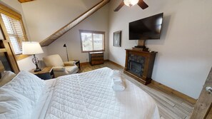 A bedroom with a large bed, a chair, a TV, a fireplace, and a window with blinds. - Paradise Found on the River - In Town - New Property - Pet Friendly (Red River)