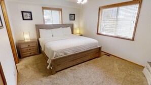 Un dormitorio con una cama de madera, dos mesitas de noche y dos ventanas con persianas.