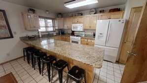 Una cocina con encimeras de granito, armarios de madera, un refrigerador, una estufa y taburetes de bar.