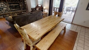 Un banco y una mesa de madera en una sala de estar con chimenea de piedra, un sofá y vistas al exterior.
