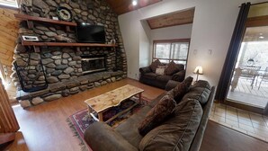 Una sala de estar acogedora con chimenea de piedra, un conjunto de sofás y un televisor montado en un estante de madera.