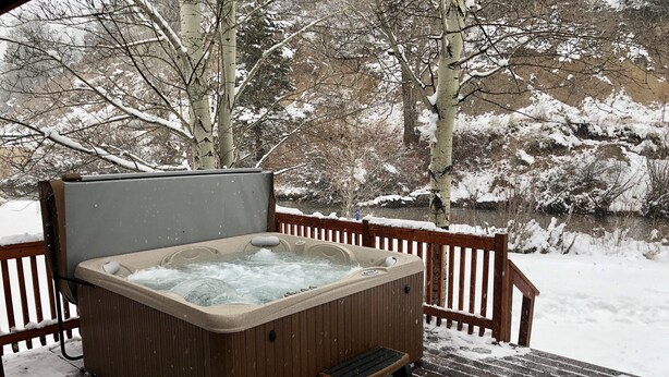 Un bain à remous sur une terrasse en bois, entouré d’un paysage enneigé.