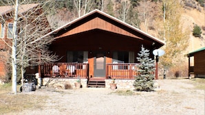 Un chalet avec une façade en bois, une véranda dotée de balustrades et des fondations en pierre.