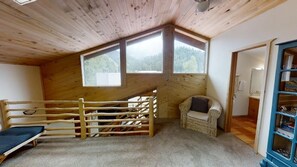 Experience a serene retreat with a view of the forest, featuring a large window and a cozy wicker chair.