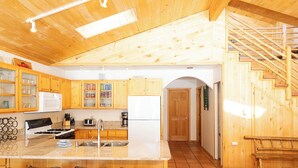 A kitchen with wooden cabinets, a white refrigerator, a stove, and a sink. There are three bar stools and a wooden bench. A staircase leads to a door. - Ski View Chalet - In Town - New Property - Pet Friendly (Red River)