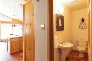 Eine Holztür führt zu einer Küche mit einem großen Fenster, einem Spülbecken und einem Spiegel darüber.