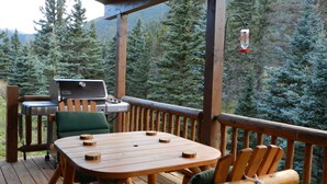 Eine Holzterrasse mit Tisch, Stühlen, einem Grill und einem Vogelhaus.