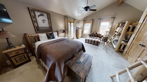 A bedroom with a large bed, a wooden bench, a dresser, a chair, and a ladder.