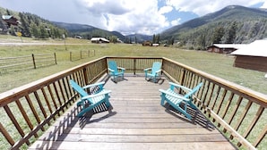 A wooden deck with two blue Adirondack chairs facing a mountainous landscape.