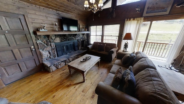 A rustic interior with a stone fireplace, wooden flooring, and a cozy seating area with a sofa and armchairs.
