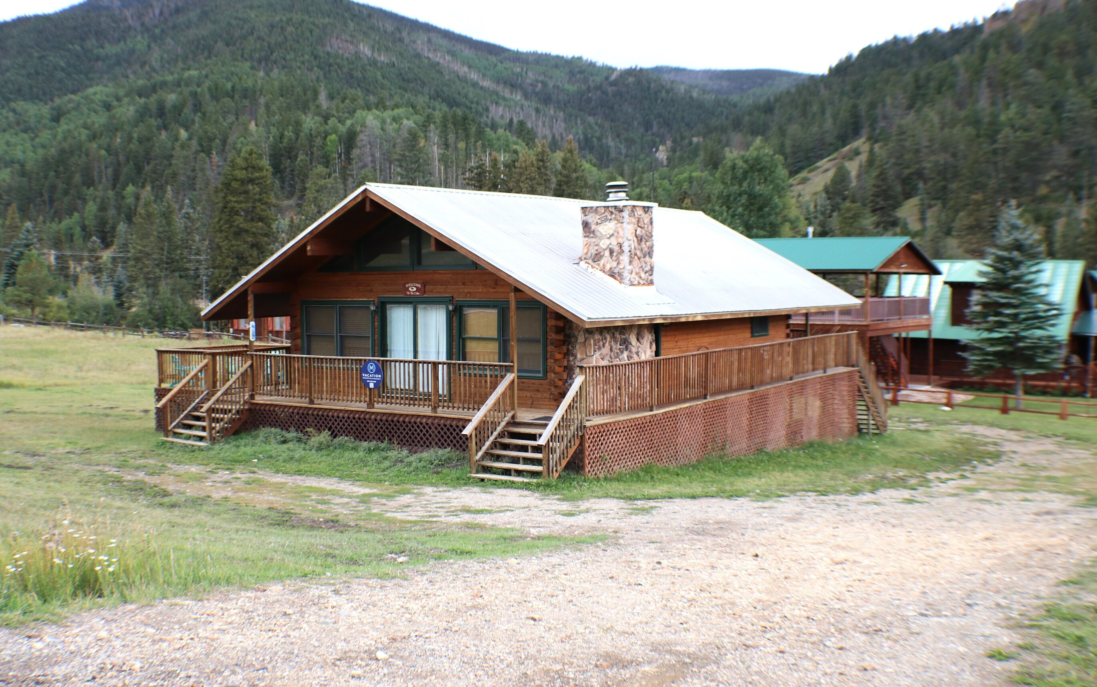 Une cabane en bois dotée d’un porche, d’une cheminée en pierre et offrant une vue sur une chaîne de montagnes boisées.