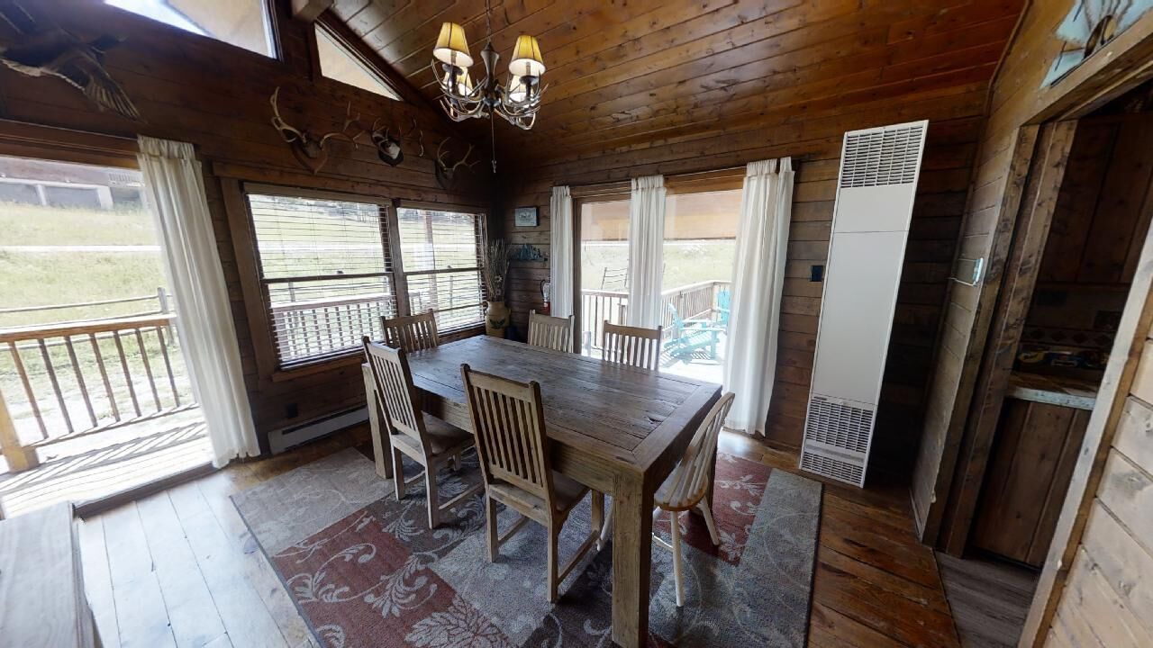 Un coin repas en bois avec une table et des chaises, de grandes fenêtres avec des rideaux et un ventilateur de plafond.