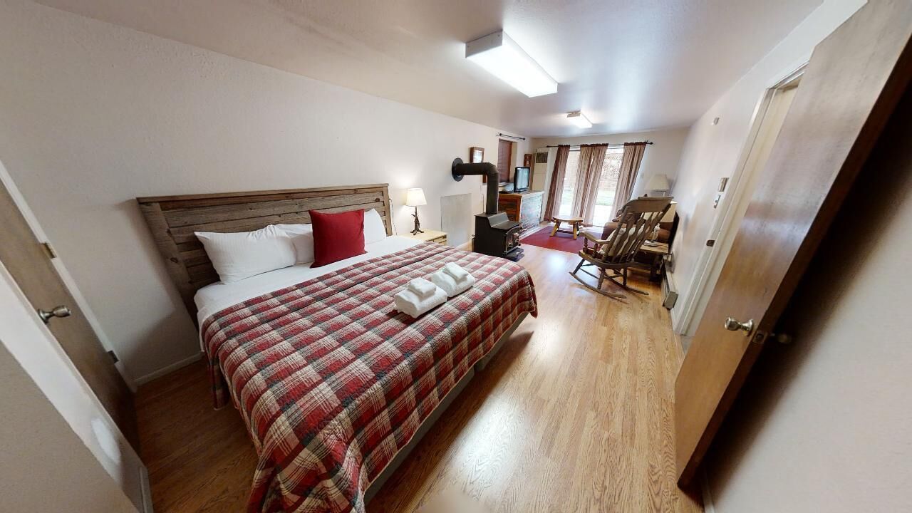 Habitación de hotel con una cama grande, cabecera de madera, escritorio con silla, televisor y ventana con cortinas.