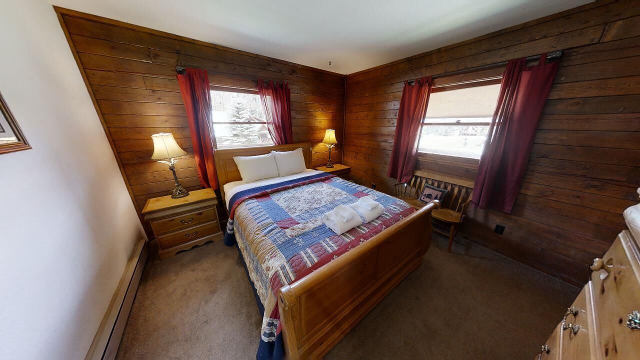 A cozy bedroom with a wooden bed, two bedside tables with lamps, and a window with curtains.