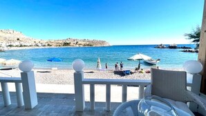 Terraço com vista para uma praia, guarda-corpo branco e uma cadeira de vime.