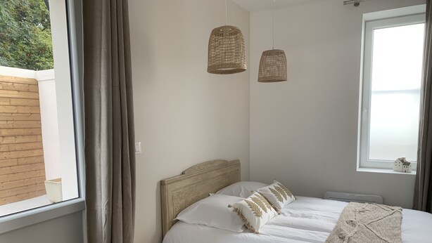 A bedroom with a bed, two hanging wicker lamps, a window with curtains, and a small wooden stool.
