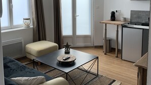 A modern apartment with a sofa, a coffee table, a dining area, a kitchen, and large windows with curtains.