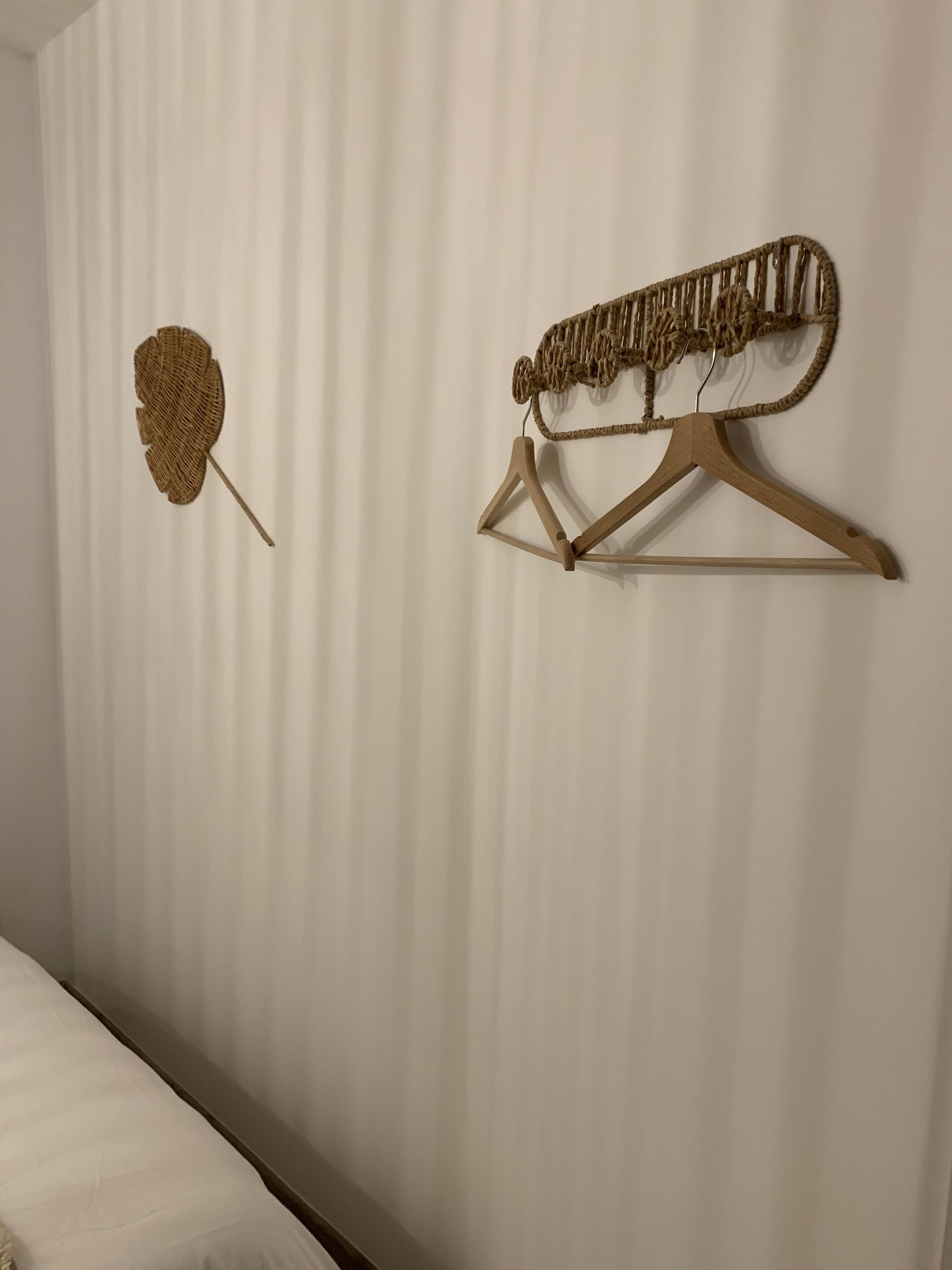 Een kamer met een bed, een houten kapstok aan de muur en een wanddecoratie van geweven materiaal.
