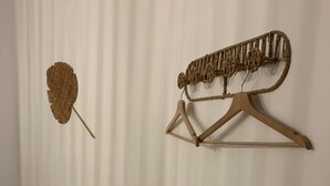 A room with a bed, a wall-mounted wooden hanger, and a woven wall decoration.