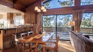 A wooden dining area with a large table and chairs, a kitchen area with a sign reading "LAKE HOUSE", and a view of trees through large windows. - ❤❤❤Tahoe Vacation Stay w/Lake Views/Next to Casinos❤❤❤ (Stateline)