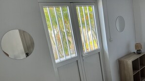 Une pièce avec une grande fenêtre, un miroir, une petite table avec une lampe et une étagère en bois.