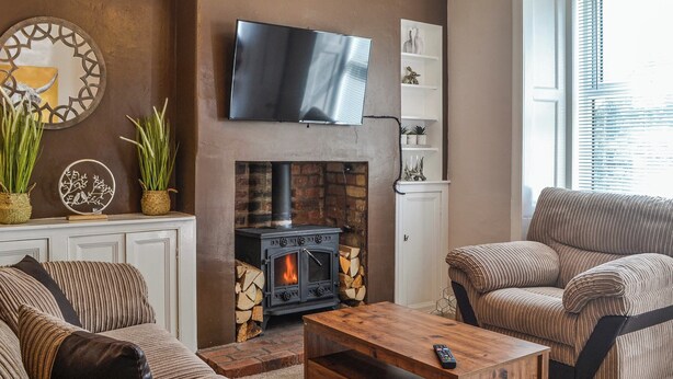 A living room with a fireplace, sofas, a coffee table, and a TV mounted on the wall. - A delightful little cottage in a peaceful village location. (New Galloway)
