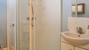 A bathroom with a glass-enclosed shower, a sink, and a mirror. - A delightful little cottage in a peaceful village location. (New Galloway)