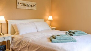 A neatly made bed with white linens, two bedside lamps, a folded towel on the bed, and a wall-mounted bird painting. - A delightful little cottage in a peaceful village location. (New Galloway)