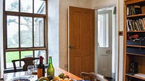 A dining area with a wooden table, a bowl of fruit, and a bookshelf with books and decorative items. - 4 bedroom accommodation in Penmachno (Penmachno)