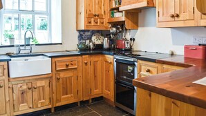 A kitchen with wooden cabinets, a sink, a stove, and a window with plants outside. - 4 bedroom accommodation in Penmachno (Penmachno)