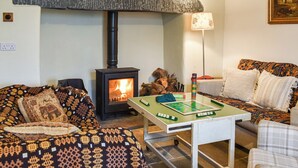 A cozy living room with a wood-burning stove, a green board game, patterned cushions, and a painting on the wall. - 4 bedroom accommodation in Penmachno (Penmachno)