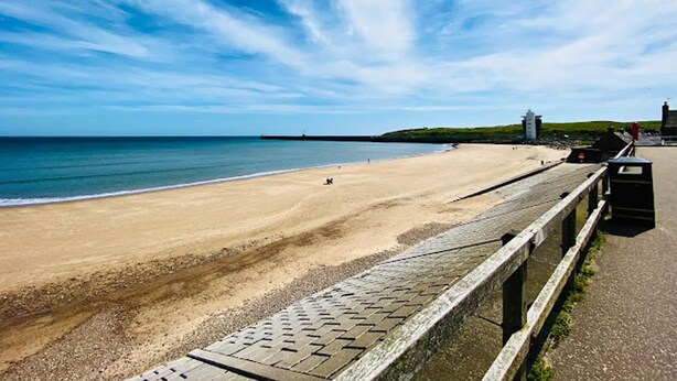 A beach with a paved walkway, a pier in the distance, and a grassy hill with buildings. - City Centre - 1 Bed - Sleeps 2 - Pet Friendly (Aberdeen)