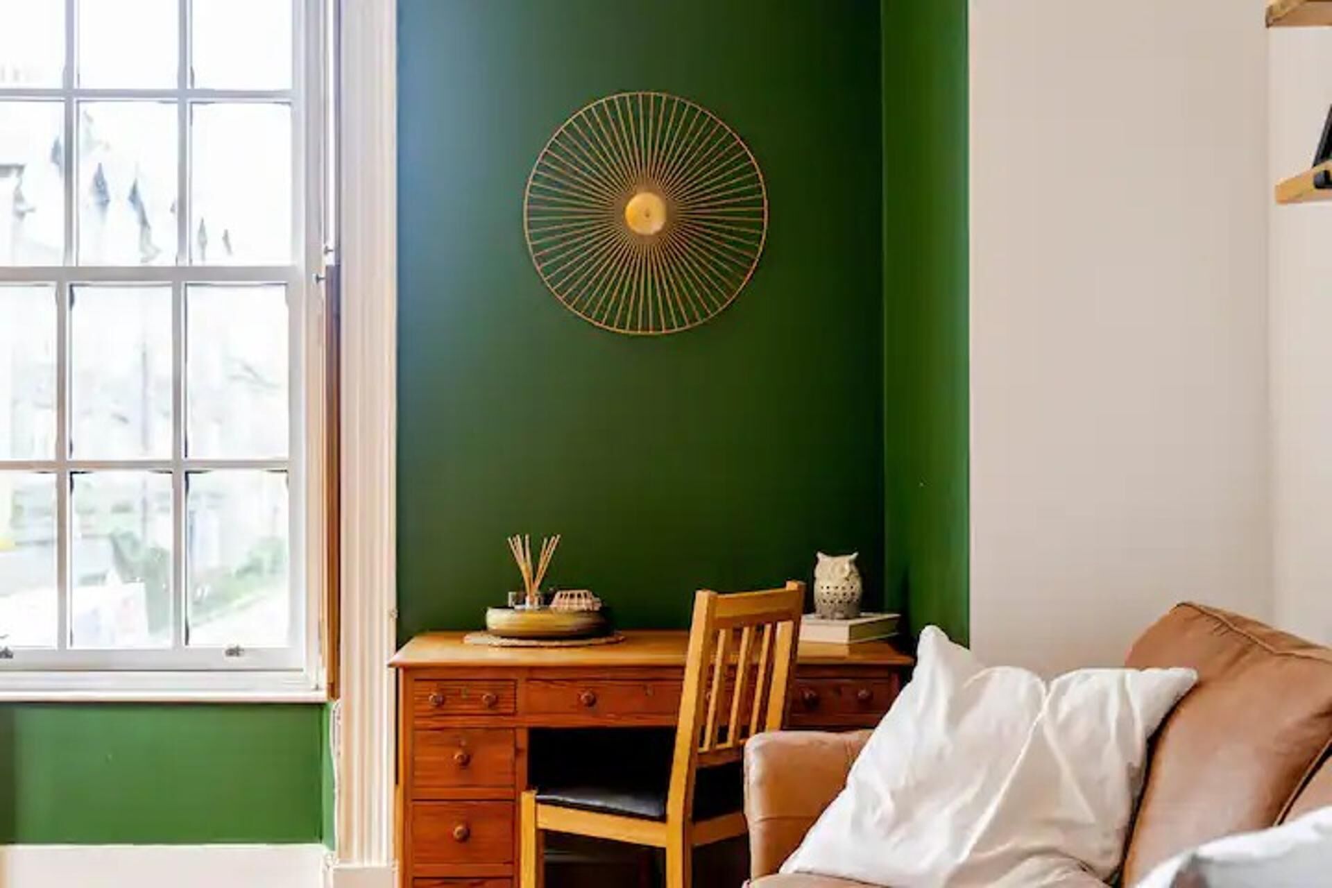 A room with a green wall, a wooden desk with drawers, a chair, and a white sofa.
