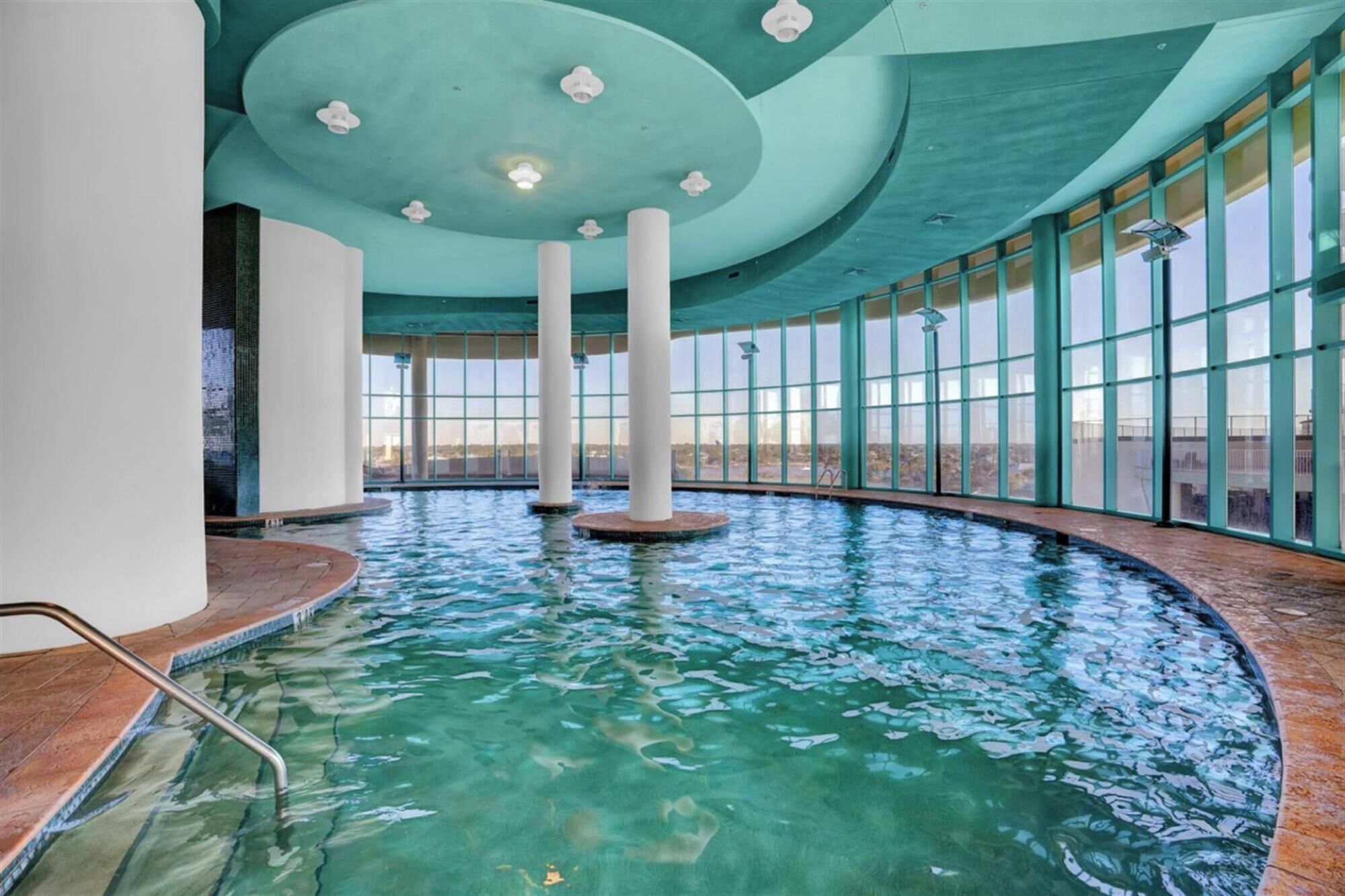 Una piscina interior con agua cristalina, ventanas amplias y techo curvo.