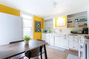 Una cocina con armarios blancos, microondas, estufa y una mesa de comedor con sillas.