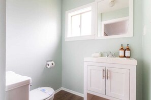 Une salle de bain avec des toilettes, un lavabo avec deux bouteilles et un miroir au-dessus du lavabo.