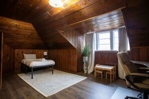 Une pièce en bois avec un lit, une petite table, une chaise et une fenêtre avec des rideaux.